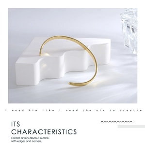Polished minimalist gold-plated cuff bracelet displayed on an artistic wave stand