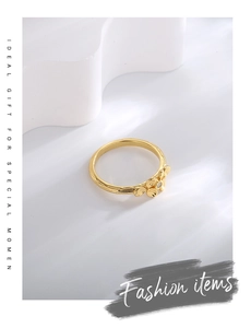 Detail of three golden flower rings with white zircon stones on a minimal white pedestal
