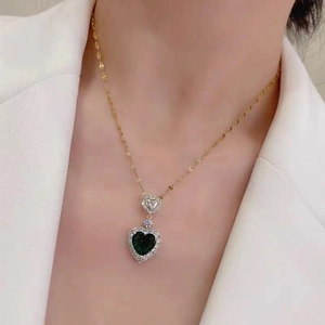 Detail of 18K gold necklace featuring a double heart pendant with emerald green stone