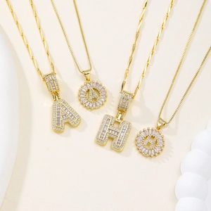 Collane con pendente 26 lettere placcate oro con zirconi su sfondo beige chiaro