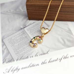 Macro detail of gold C letter pendant with colorful gemstones on dark wood jewelry box