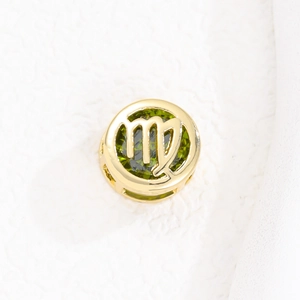 Detalle del colgante zodiaco Virgo dorado con gema verde sobre fondo blanco puro