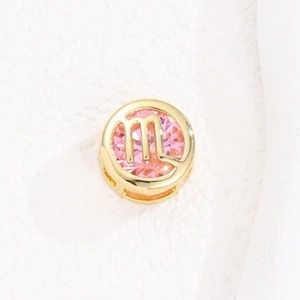 Detalle del colgante de Virgo dorado con piedra rosa facetada y símbolo de la letra m