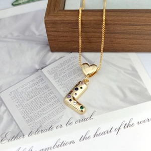 Macro detail of gold-plated L letter pendant with colorful cubic zirconia and heart bail