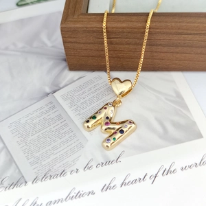 Close-up of golden letter M pendant with colorful zircon stones and heart clasp