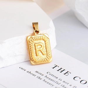 Macro-opname van een gouden rechthoekige hanger met letter R en zonnestraalmotief