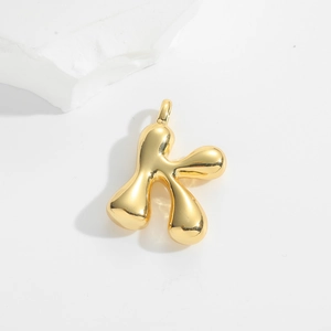 Detailed view of bubble initial K pendant with smooth gold metallic finish on white rock