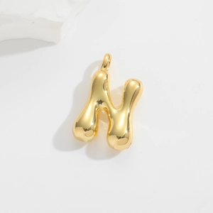 Detailed macro view of a 3D bubble style golden letter H pendant on a white stone background
