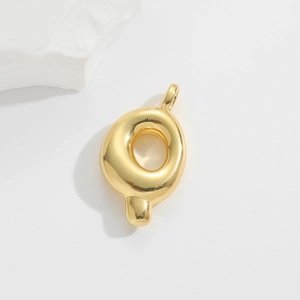 Macro detail of glossy gold puffed alphabet Q pendant on a minimalist white stone background