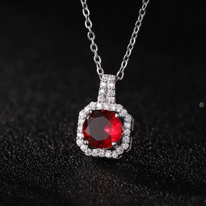 Collier chaîne argentée avec pendentif zircon rouge rond et sertissage halo sur fond noir
