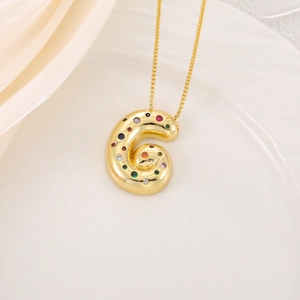 Gros plan du pendentif lettre G dorée avec zircons colorés sur un fond en soie