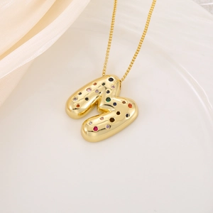 Détail d'un pendentif lettre M 3D doré serti de zircons colorés sur une fine chaîne