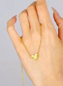 Macro detail of gold plated heart pendant with engraved letter G on fine link chain