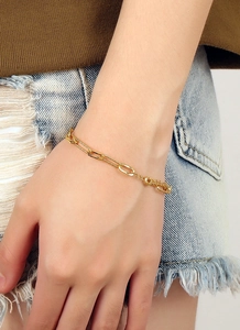 Gros plan d'un bracelet trombone plaqué or porté au poignet avec une tenue décontractée