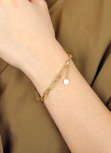 Détail d'un bracelet doré double couche avec chaîne trombone et petit pendentif rond brillant