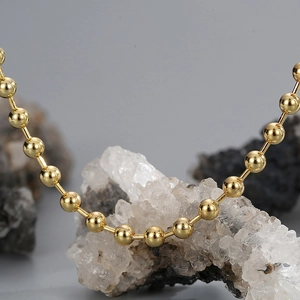 Polished gold beaded ball chain necklace draped on a natural raw white stone crystal