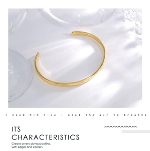 Detail of a minimalist gold-plated cuff bracelet featuring delicate engraved patterns