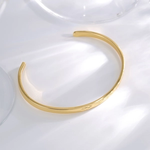 Golden open C-shaped cuff bracelet with minimalist engraved patterns on white background