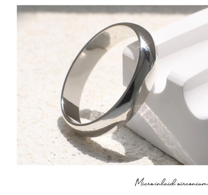 Anello minimalista in argento lucido su supporto geometrico con luce naturale