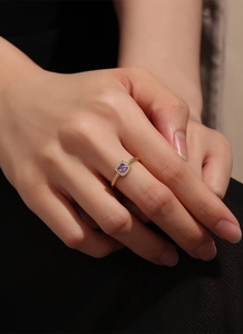 Detail of gold ring featuring a square purple zircon center stone with a halo of white gems