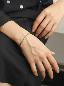 Detalle de un brazalete ajustable chapado en oro de 18K con diseño de engranaje en la muñeca