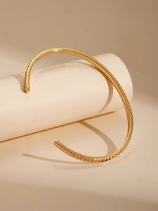Detalle de la pulsera rígida chapada en oro de 18K con textura ondulada y diseño abierto
