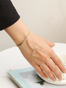 Primer plano de una pulsera minimalista bañada en oro de 18K usada por una modelo en la muñeca