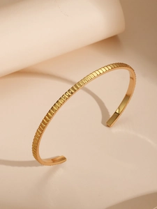 Detalle de brazalete minimalista bañado en oro de 18K con textura acanalada vertical
