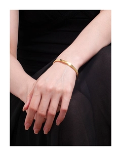 Gros plan d'un bracelet ouvert doré minimaliste avec une finition polie sur un poignet