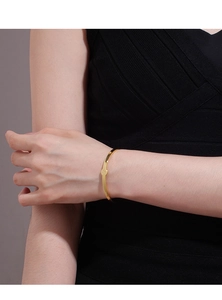 Detailaufnahme eines minimalistischen goldenen Armreifs mit Herz und Gravur des Buchstabens A