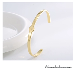 Detail eines goldenen Armreifs mit minimalistischem runden Anhänger und graviertem A