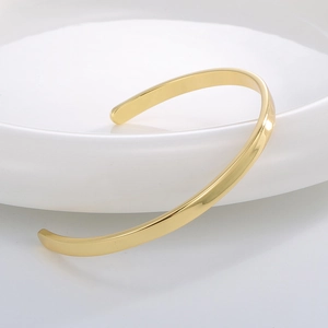 Bracelet jonc ouvert minimaliste doré poli posé sur une assiette en céramique blanche