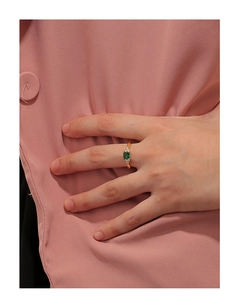 Dettaglio di un anello placcato oro con pietra verde rettangolare al dito