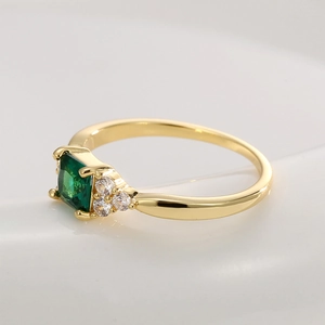 Anello dorato elegante con zircone verde quadrato e cristalli su uno sfondo bianco