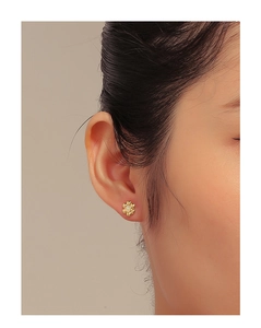 Close-up of a floral gold stud earring with opal stone worn on the earlobe