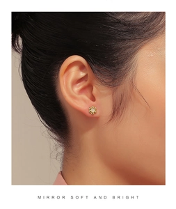 Close-up of golden flower stud earring with white pearl center on a female model