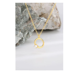 Detailansicht einer goldenen Kreishalskette mit klarem Zirkon auf einem Naturstein