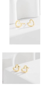 Macro shot of gold hollow heart stud earrings on a minimalist white stone display