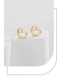 Macro shot of minimalist gold heart stud earrings on a white geometric display stand