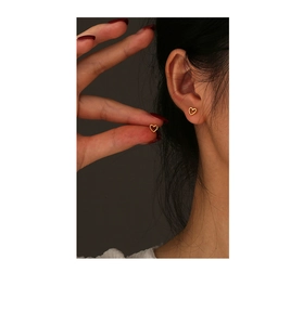 Close-up of small golden heart stud earrings in S925 silver on a model's ear