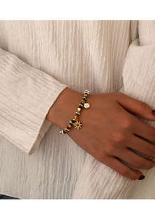 Dettaglio del bracciale di perle con ciondolo a stella e pietre verdi su fondo bianco