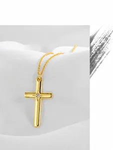 Detail eines goldenen Kreuzanhängers mit rundem Zirkon und polierter Spiegeloberfläche