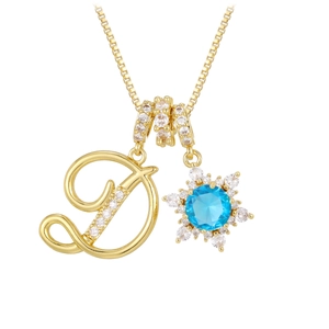 Macro detail of gold-tone necklace featuring D-letter pendant and blue crystal snowflake