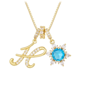 Macro shot of 18K gold plated letter H pendant with zircon stones and blue sunburst gem