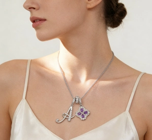Detail of silver chain necklace with letter A pendant and purple gemstone clover