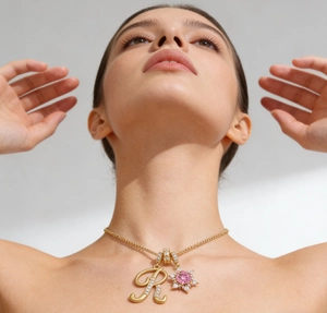 Detalle del collar dorado con colgante letra R y circonita de girasol rosa en el cuello