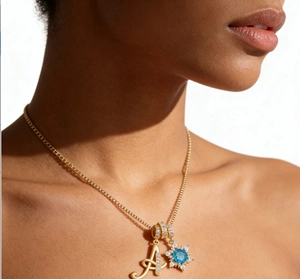 Detail of gold necklace with zircon letter A and blue stone snowflake pendant