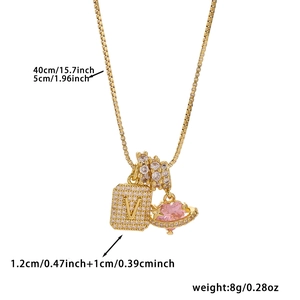 Detail view of gold square letter V pendant and pink heart saturn charm with zircons