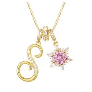 Macro detail of golden necklace with crystal S letter and pink snowflake pendant