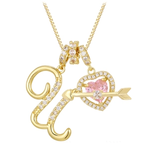 Macro detail of gold necklace with pink heart gem, arrow pendant and zircon crystal letter